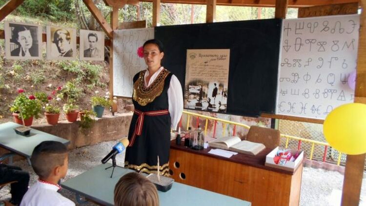 Учителка с народна носия преподава в класна стая на открито